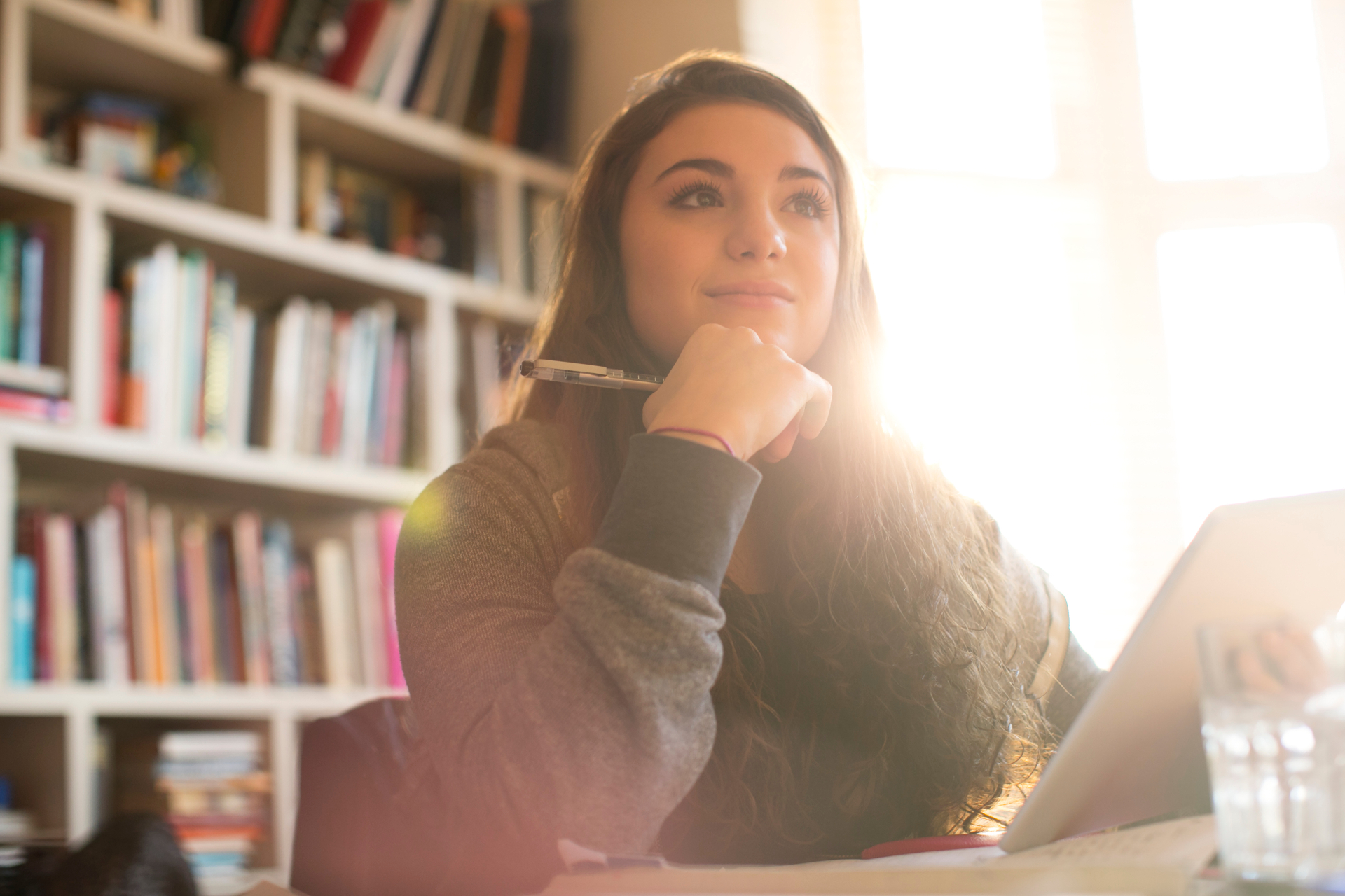 Student smiling thoughtfully while studying with a laptop in a sunlit library